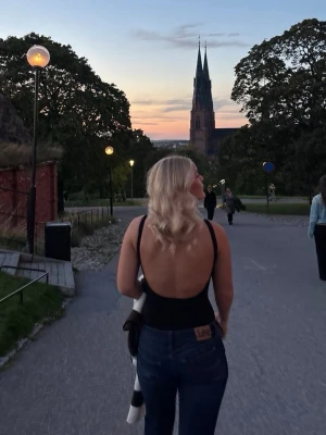 Svart body med djup rygg - Säljer en svart body med breda axelband och riktigt djup, öppen rygg. Bodyn har en enkel, stilren design och är tillverkad i ett stretchigt material som sitter snyggt på kroppen. Perfekt att matcha med jeans eller kjol för en trendig look.