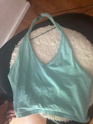 Ljusblå croppad linnetopp - Säljer en ljusblå croppad linnetopp med halterneck och v-ringning. Toppen är ärmlös och har en enkel, stilren design som passar perfekt till sommaren. Superskön och lätt att matcha med jeans eller kjol.