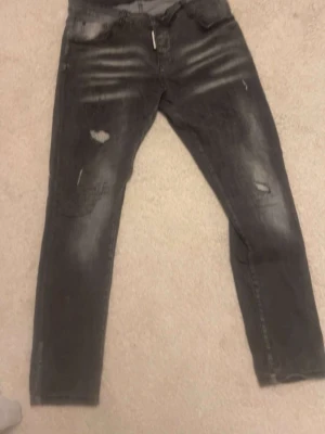 mörkgråa dsq2 jeans - Säljer ett par grå skinny jeans med slitningar och hål på knäna. Jeansen har en tvättad look och klassisk femficksmodell. Materialet är troligtvis bomull med stretch för extra komfort. Perfekta för en avslappnad och trendig stil.