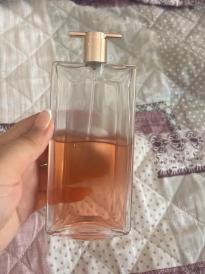 Lancome parfym med roséguld-detaljer - Säljer en elegant parfym från Lancome i en rektangulär glasflaska med roséguld-färgat lock och detaljer. Flaskan har en ljusrosa doftvätska och en stilren, modern design som känns lyxig och trendig.
