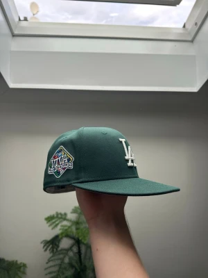 Grön LA Dodgers keps - Snygg grön 59fifthy keps från New Era med LA Dodgers-logga framtill i vitt och broderad patch på sidan.  Säljer för att den var för liten för mig. Köpte från topperzstore för 549 kr. Aldrig använd.