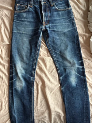 Blå lean dean jeans selvage - Säljer ett par blå jeans med raka ben och snygga slitningar på låren och knäna. Jeansen har klassisk femficksmodell, orangea sömmar och knappgylf. Perfekta för en avslappnad och trendig look.