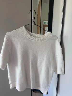 Vit croppad stickad topp - Säljer en vit croppad stickad topp med korta ärmar och rund hals. 