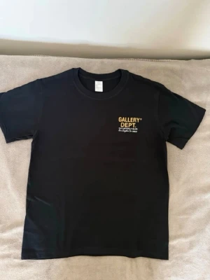 Gallery Dept tisha - Snygg svart t-shirt från Gallery Dept med gul logga och text på bröstet. Klassisk rund hals och korta ärmar. Perfekt för dig som gillar streetwear och enkel stil.