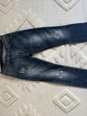 Blå nudie jeans (Thin Finn) - Säljer ett par blå nudie jeans modell thin Finn med slitningar och hål på både fram- och baksida har även snygga patchwork på både fram-och baksida. Jeansen har en tvättad look, en blandning av slim och straight fit. Hör av er vid intresse. Vid snabb affär kan jag gå ner i pris!