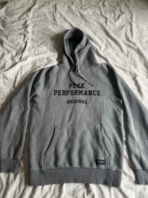 Grå Peak Performance hoodie - Snygg grå hoodie från Peak Performance med svart text på bröstet. I ett väldigt bra skick.
