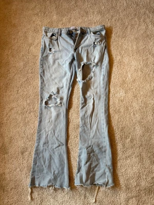 Ljusblå slitna jeans från ZARA - Säljer ett par ljusblå jeans från ZARA med flera slitningar och hål på benen