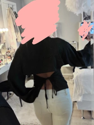 Svart topp med öppen rygg och snörning - Säljer en svart topp med vida ärmar och öppen rygg som knyts med snörning. Från Nelly i storlek 36