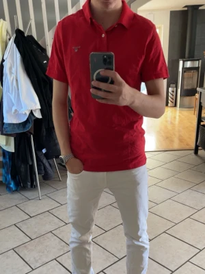 Röd Gant piké t-shirt - Röd piké t-shirt från Gant med klassisk krage och två knappar. Kortärmad modell i mjuk bomull med liten broderad logga på bröstet. Perfekt för en enkel och stilren outfit.
