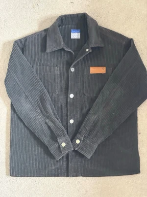 Mörkgrön/svart overshirt Jacob Cohen - Snygg svart overshirt från Jacob Cohen. Skjortan har klassisk krage, bröstficka och knappar framtill. Perfekt lager-på-lager-plagg med en stilren look och diskret läderdetalj på bröstet.