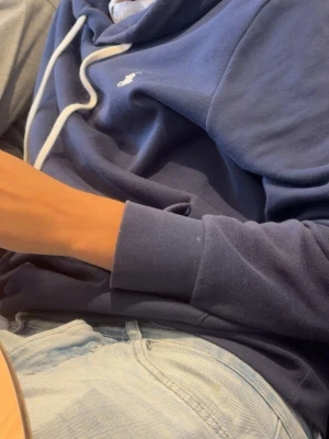 Mörkblå hoodie med vit logga - Snygg mörkblå hoodie med vit dragsko och liten vit logga på bröstet. Hoodien har klassisk huva och ribbade muddar vid ärmsluten. Perfekt för en avslappnad och trendig stil. Materialet ser ut att vara mjukt och bekvämt, troligen bomull eller bomullsblandning.