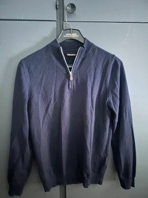 Mörkblå stenströms half zip  - Mörkblå stickad tröja med lång ärm och halv dragkedja framtill. Tröjan har ribbade muddar vid ärmslut och nederkant samt en stilren, enkel design. Perfekt för lager på lager och passar till det mesta. Super fin half zip från stensteöms, ett exklusivt märke.