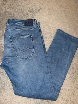 Ljusblå jeans från Replay - Säljer ett par ljusblå jeans från Replay med klassisk femficksdesign och diskret broderad detalj på bakfickan. Jeansen har rak passform och är tillverkade i mjukt denimtyg. Perfekta för en avslappnad och stilren look.Ny pris 1799