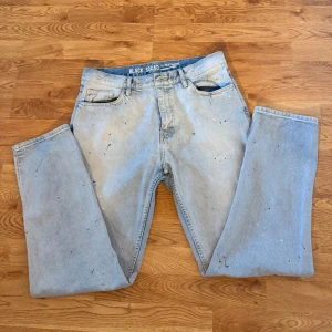 Ljusblå jeans med färgstänk - Säljer ett par ljusblå jeans med coola färgstänk och en avslappnad passform. Perfekta för en streetwear-look.            Storlek:30/32