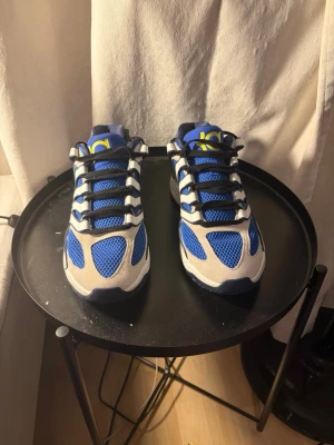 Blå och vita NIKE KD 18 - NIKE KD 18 i blått och vitt med meshpaneler för extra ventilation. Skorna har svarta snören, vita och grå detaljer samt gula accenter på plösen och sidan. Sulan är vit och designen är sportig och modern. Knappt använda och är en väldigt bra skor generellt. STORLEK 45. Kommer med KOBE BOX på de också.