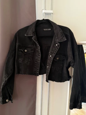 Jeansjacka  - Svart cropped jeansjacka från DILVIN i fint skick. Snygg och trendig modell med kort passform och detaljerad design. Säljes då den inte längre kommer till användning.  Katt finns i hemmet, produkten rollas av så gott det går.