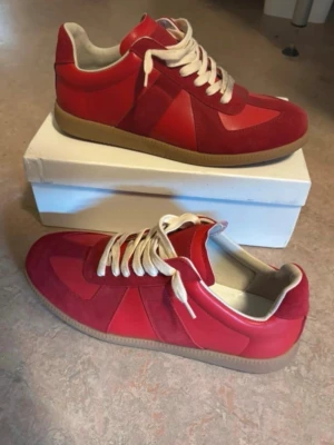 Röda maison margiela gats - Snygga röda sneakers med beige sula och vita skosnören. Skorna har en mix av mocka och slätare material på ovandelen, vilket ger en schysst kontrast. Låg modell som passar perfekt till jeans eller streetwear. Klassisk siluett med modern touch.
