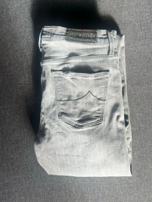 Jacob Cohen jeans - Snygga ljusgrå jeans från Jacob Cohen med klassisk femficksmodell och diskreta sömmar. Jeansen har en patch med logga bak i midjan och silverfärgade detaljer. Perfekta för en stilren och avslappnad look.
