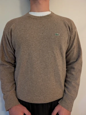 Lacoste tröja gråbrun, stl M - Lacoste stickad tröja i gråbrun med den klassiska krokodillogotypen på bröstet, stl M. Bra basplagg, sitter skönt. Fint skick rakt igenom. Modell: 182cm | 83kg.