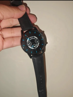 Svart klocka med blå detaljer - Stilren svart klocka från Geneva med rund urtavla och blå markeringar. Klockan har ett svart band i syntetmaterial och en cool design på urtavlan med vita och blå detaljer. Perfekt accessoar för dig som vill ha en modern look.