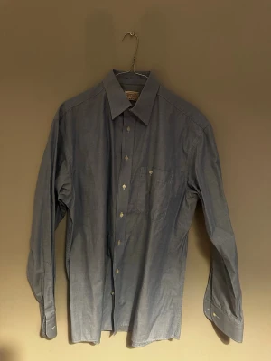 Blå klassisk skjorta  - Säljer en stilren blå skjorta från Eton med klassisk krage och bröstficka. Skjortan framtill. Perfekt till jeans eller chinos i storlek 44 alltså L/XL