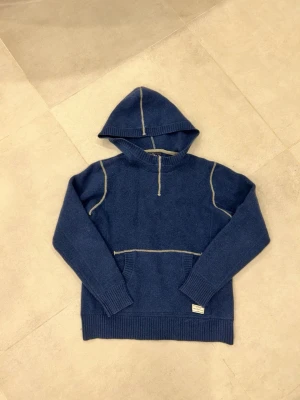 Blå hoodie från Peak Performance - Mysig blå hoodie från Peak Performance med kontrastsömmar i vitt. Hoodien har en stor huva, ribbade muddar och en klassisk känguruficka framtill. Tillverkad i mjukt material som känns skönt mot huden. Perfekt för en avslappnad och cool stil. Den krympte i tvätten så att nu är de storlek xs istället.