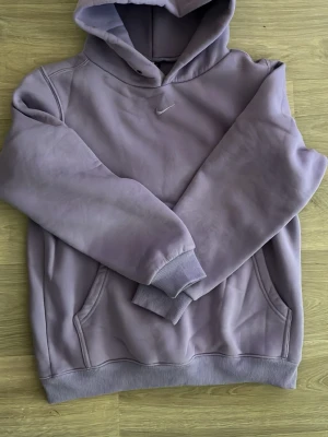 Ljuslila hoodie Nike - Säljer en ljuslila hoodie från Nike med broderad vit Swoosh-logga på bröstet. Hoodien har huva, känguruficka och ribbade muddar vid ärmslut och nederkant. Tillverkad i mjukt bomullsmaterial som är skönt mot huden.