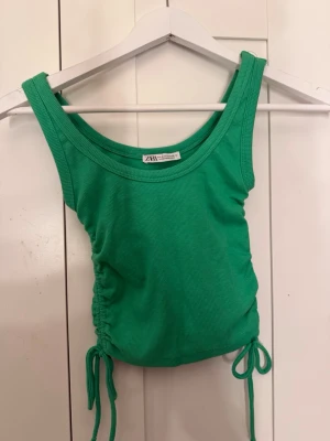 Grön ribbad linnetopp från Zara - Snygg grön ribbad linnetopp från Zara med knytband i sidorna och rund halsringning. Toppen är ärmlös och har en croppad passform som ger en trendig look. Perfekt att styla med jeans eller kjol för en cool outfit.