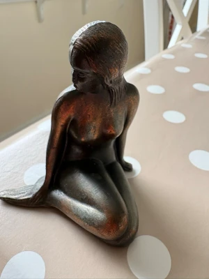 Metallstatyett sjöjungfru - Dekorativ statyett i metall föreställande en sittande sjöjungfru. Figuren har en mörk bronsliknande färg med lätt kopparskimmer och fina detaljer i håret och fenan. Perfekt som prydnad i hemmet. Höjd: 10 cm.                               Kolla gärna mina andra annonser ❗️