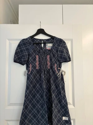 Blårutig klänning/lång blus Odd Molly - Supersöt blårutig klänning/lång blus från Odd Molly med kort ärm, rosa broderier och snörning i midjan. Klänningen har v-ringning och fina detaljer som ger en unik look. 