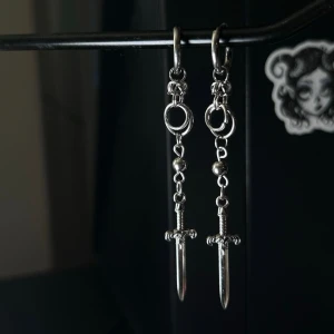 Handmade sword earrings in stainless steel, alternative style  - 🕷️Handmade earrings by me ⛓️Material: Stainless Steel 🖤Length 8cm  🖤Jewerly care:  – Avoid longer contact with water – Avoid excessive perfume, lotions, and chemicals – Do not sleep or exercise while wearing  Proper care helps maintain appearance and longevity ✨  Feel free to check out my other pieces- bundle discounts available💸  The price list is set based on material costs, my working hours and based on unique designs and other costs.