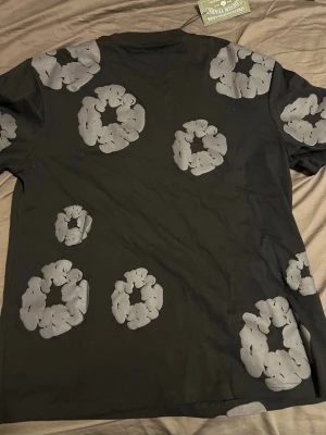 Svart t-shirt med grått blommönster - Cool svart t-shirt  med unikt grått blommönster över hela tröjan. Klassisk rund halsringning och korta ärmar. Perfekt för dig som vill sticka ut med en streetwear vibe.