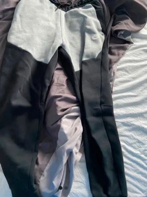 Nike tvåfärgade mjukisbyxor - Snygga mjukisbyxor från Nike i svart och ljusgrått. Byxorna har dragsko i midjan och en liten Nike-logga på ena benet. Tillverkade i mjukt sweatshirtmaterial som är perfekt för chill dagar. Raka ben och klassisk passform.