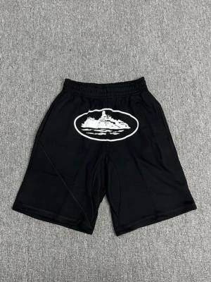 Svarta shorts med tryck - Svarta shorts med elastisk midja och ett stort vitt tryck framtill. De har en avslappnad passform och är perfekta för en chill stil. Materialet känns lätt och bekvämt, perfekt för varma dagar.