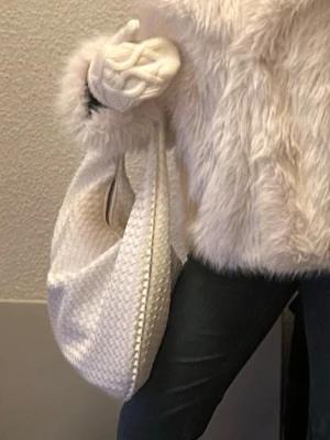 Vit flätad axelväska - Säljer en stor och mjuk axelväska i vit färg med flätad struktur. Väskan har en rundad form och bred axelrem, vilket gör den snygg och praktisk. 