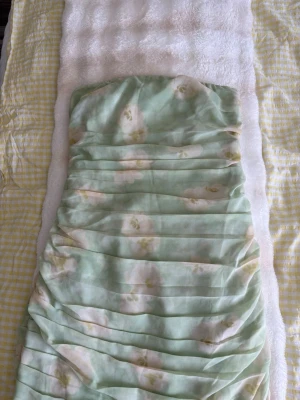 Ljusgrön axelbandslös långklänning - Säljer en romantisk ljusgrön långklänning med blommigt mönster och draperad design. Klänningen är axelbandslös och har en mjuk, flowy känsla som passar perfekt till sommarens alla tillfällen.