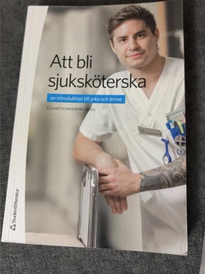 Att bli sjuksköterska bok - Boken 'Att bli sjuksköterska: en introduktion till yrke och ämne' har ett omslag med en person i vit vårdklädsel och blå detaljer. Boken är tryckt på vanligt papper och har ett mjukt omslag. Perfekt för dig som vill plugga till sjuksköterska.