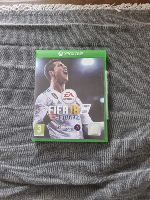 FIFA 18 till Xbox One - FIFA 18 till Xbox One med grön plastfodral. Omslaget visar en fotbollsspelare i vit matchtröja och spelet är utvecklat av EA Sports. Perfekt för dig som gillar sportspel och fotboll.