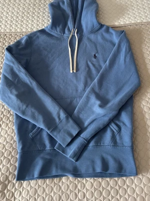 Blå hoodie från Polo Ralph Lauren - Snygg blå hoodie från Polo Ralph Lauren med klassisk huva och vita dragsnören. Broderad logga på bröstet. Perfekt passform mycket bra skick använd 4-5 gånger 
