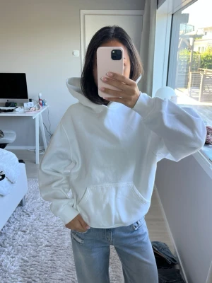 Vit oversized hoodie - Säljer en vit oversized hoodie med stor huva och magficka. Hoodien har en clean look utan tryck eller logga, ribbade muddar vid ärmar och nederkant samt mjukt material. 