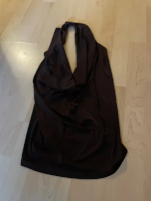 Brun omlott halterneck topp - Snygg brun halterneck topp med omlott-detalj och djup v-ringning. Tunt och mjukt material som faller snyggt. Perfekt för att skapa en trendig och stilren look.