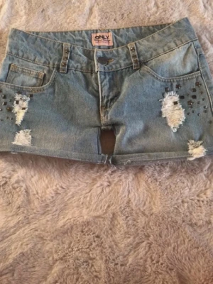 Ljusblå jeansshorts med nitar från ONLY - Snygga blå jeansshorts med slitna detaljer och coola metallnitar fram och bak. Klassisk låg midja och insydda ben för fin passform. Perfekta till sommaren, bekväma och trendiga. Hör av er vid frågor. Priset är inte hugget i sten! Kolla gärna in om du hittar något annat kan du få mängdrabatt 💕