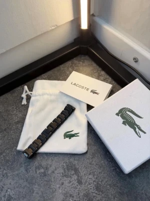 Svart lacoste armband  - Svart Lacoste-armband i snygg metall-design. Mycket fint skick och kommer med originalbox samt påse. En stilren detalj som passar till alla outfits. Pris kan diskuteras vid snabb affär.