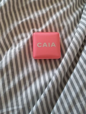 CAIA rosa rouge i kompakt dosa - Säljer ett rouge från CAIA i en snygg rosa kompakt dosa med spegel. Rouget har en mjuk rosa nyans och kommer i puderform, perfekt för att ge kinderna en fräsch färg. Dosan är fyrkantig och smidig att ta med i väskan.