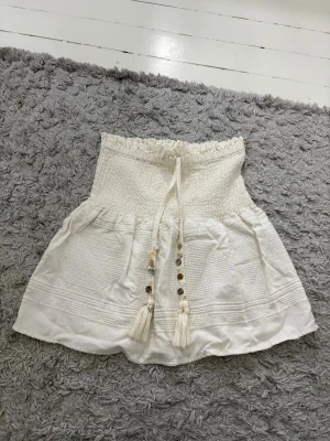 Krämvit kjol med snörning och pärlor - Supersöt vit kortkjol med smock i midjan och snörning framtill dekorerad med pärlor. Kjolen har fina detaljer i tyget. Går att använda både som kjol och tub topp💞Dessvärre värkar jag ha klippt bort lappen men skulle gissa på att den är i storlek S💞