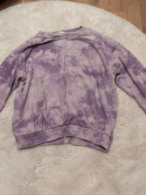 Lila tie-dye sweatshirt - Säljer en lila sweatshirt från Lindex. Tröjan har ett snyggt tie-dye mönster i olika lila nyanser och breda muddar vid ärmslut och nederkant. Perfekt för dig som gillar en avslappnad och trendig stil.