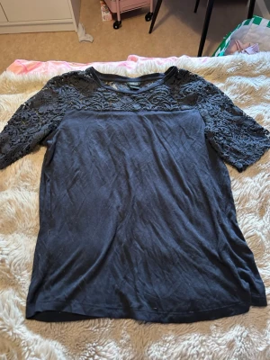 Blå topp med spetsdetaljer - Snygg blå topp med halvärmade spetsdetaljer över axlar och ärmar. Toppen har rund halsringning och är tillverkad i mjukt material med dekorativ spets upptill som ger en elegant touch.