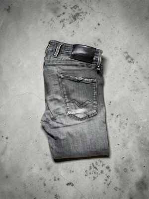 Gråa slim fit jeans med slitningar - Snygga grå jeans i slim fit-modell med slitna detaljer och klassisk femficksdesign. Jeansen har en tvättad look och tydliga sömmar på bakfickan. Perfekta för en avslappnad och trendig stil.