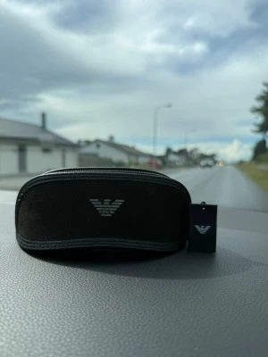 Emporio Armani svarta solglasögon - Snygga svarta solglasögon från Emporio Armani med rektangulära linser och tunna metallbågar. Kommer med originalfodral och tagg. Perfekt accessoar för en stilren look.