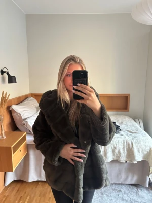Mörkbrun fuskpälsjacka med huva - Säljer en fluffig mörkbrun fuskpälsjacka från Realty med stor huva och knäppning framtill. Jackan har en oversized passform och är perfekt för kalla vinterdagar. Supermjuk och ger en lyxig känsla till din outfit.
